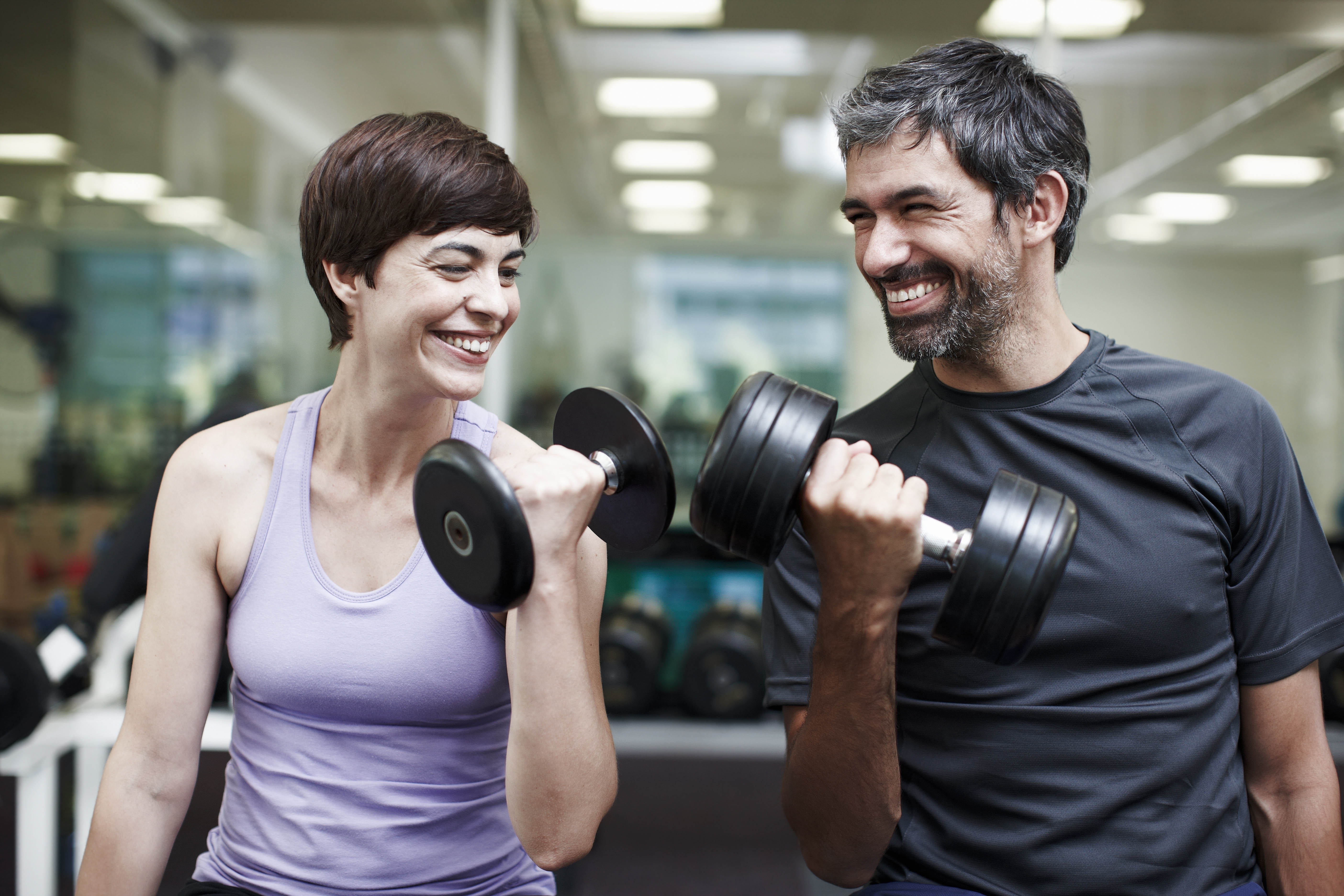 Smiling couple working out together in the gym, lifting free weights Smiling couple working out together in the gym, lifting free weights